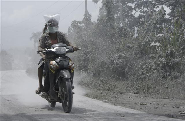 Người dân làng đội bì nilon lên đầu và đeo khẩu trang khi chạy xe máy trên một con đường phủ đầy tro bụi núi lửa ở Kuta Mbaru, Bắc Sumatra