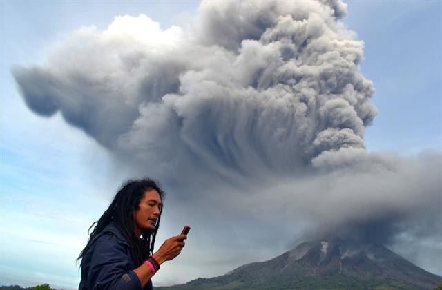 Một người đàn ông sử dụng điện thoại di động khi ngọn núi lửa Sinabung tiếp tục phun trào với những cột khí nóng khổng lồ, ở quận Karo