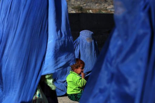 Một đứa trẻ Afghanistan mặc quần áo màu xanh lá cây gần mẹ của mình khi người phụ nữ này đang cầu nguyện cùng nhiều phụ nữ khác