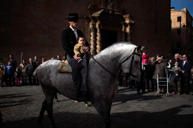 Một người cha ẵm đứa con đi ngựa ngang qua nhà thờ Santa Maria, khi họ tham gia lữ mừng ngày Thánh Anthony the Abbot, vị thánh bảo trợ cho các loài động vật trong vùng, ở Caldas de Montbui, gần Barcelona