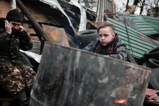 Một đứa trẻ ấm lên nhờ một ngọn lửa thắp sáng sau một chướng ngại vật ở trung tâm Kiev - Ukraine