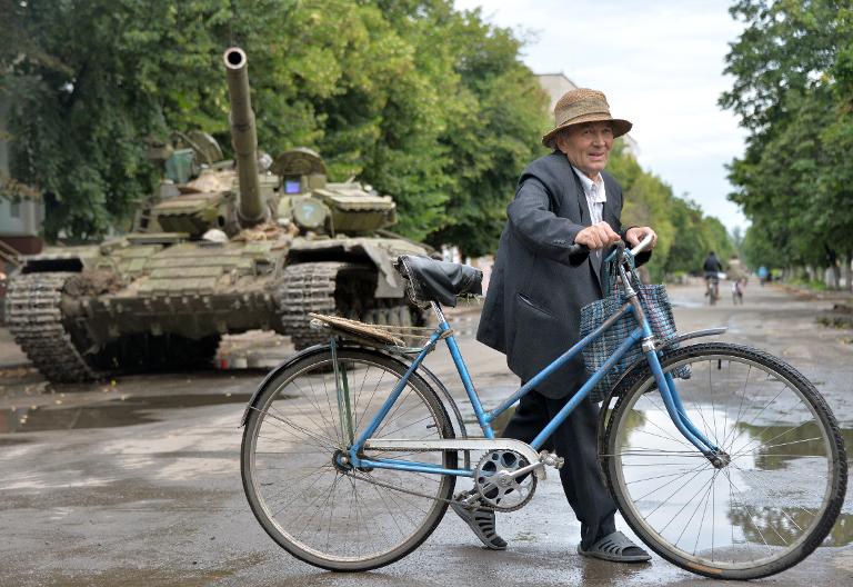 Một cư dân địa phương đang dắt xe đạp ngang qua một chiếc xe tăng Ukraina ở thành phố Slavyansk phía đông của Ukraina