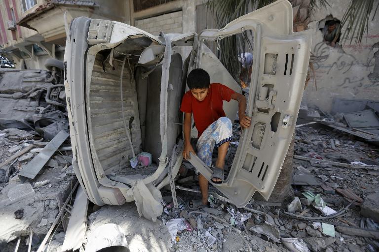 Một cậu bé Palestine và phần còn lại của một chiếc xe sau một cuộc không kích của Israel tại Dải Gaza