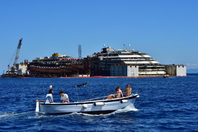 Một chiếc thuyền nhỏ chở khách du lịch đi ngang qua xác con tàu du lịch Costa Concordia ngoài khơi bờ biển của đảo Giglio, Italy