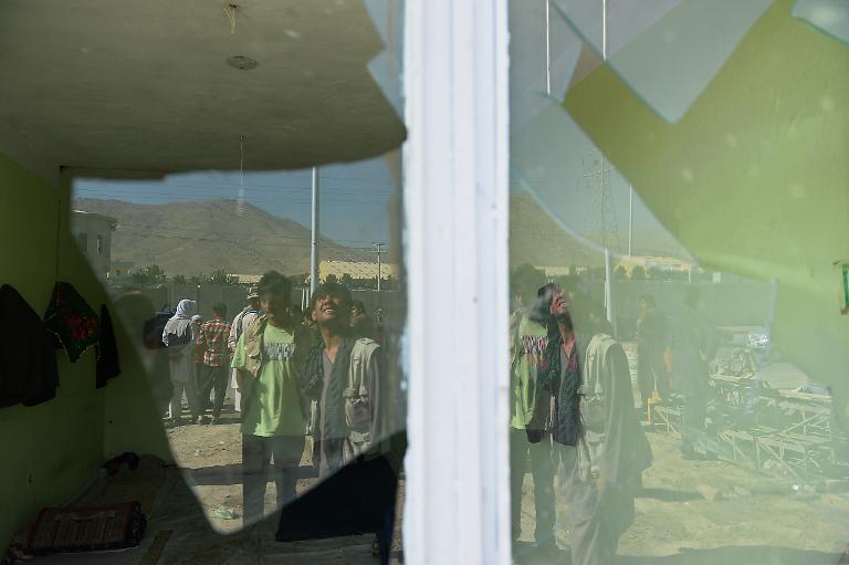 Hình ảnh phản chiếu qua tấm kính vỡ cho thấy những người dân Afghanistan tại hiện trường của một cuộc tấn công tự sát ở Kabul