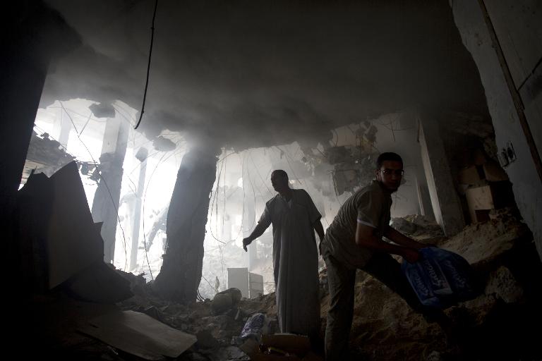 Những người đàn ông Palestine đang dọn dẹp đống đổ nát ở tầng trệt của một tòa nhà trúng đạn pháo trong cuộc không kích của Israel vào thành phố Gaza