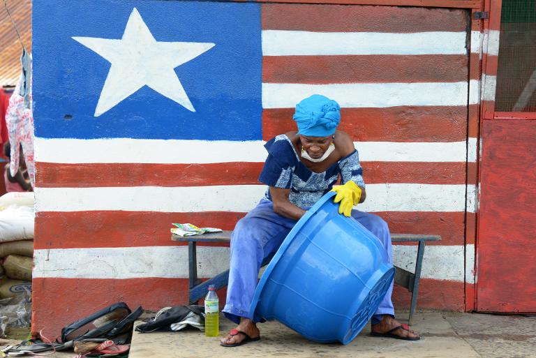 Một người phụ nữ đang vệ sinh các vật dụng phía trước bức tường in hình quốc kỳ Liberia