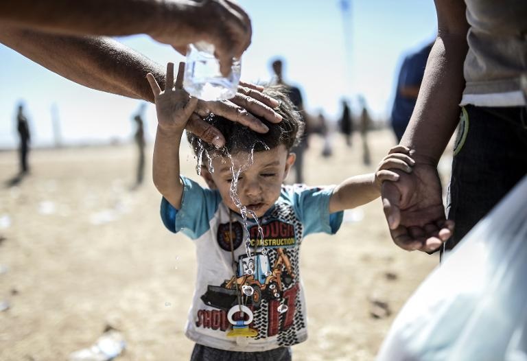Một đứa trẻ người Kurd Syria được đổ nước làm mát sau khi vượt qua biên giới giữa Syria và Thổ Nhĩ Kỳ, gần thị trấn phía đông nam Suruc ở tỉnh Sanliurfa, Syria