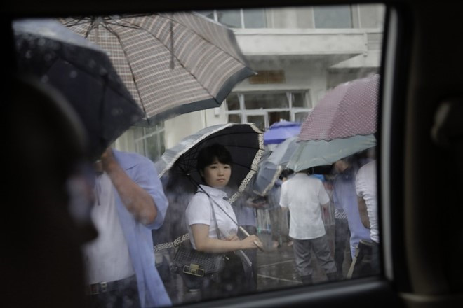 Người phụ nữ xếp hàng đợi xe buýt trong mưa ở Bình Nhưỡng.