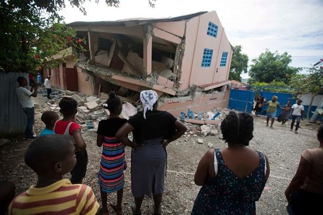 Những người dân địa phương đứng trước một ngôi trường đổ sập ở Gros Morne, Haiti trong trận động đất ngày 7/10. Các nhân viên cứu trợ đã được điều động tới, gấp rút khắc phục thảm họa. Ảnh: AP 