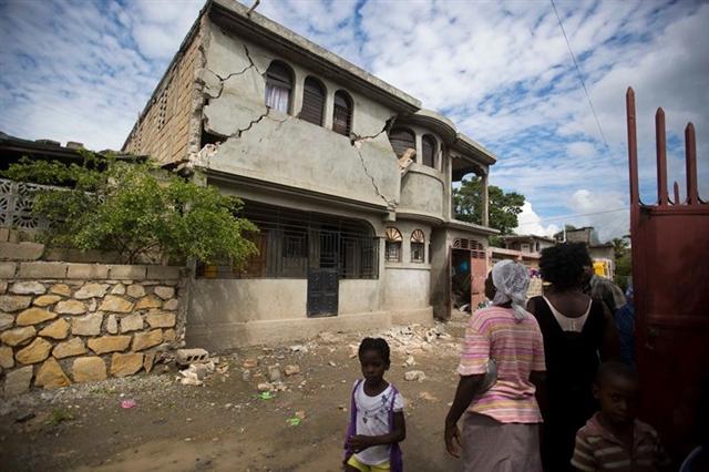 Người dân đứng nhìn một ngôi nhà loang lổ những vết nứt sau trận động đất ngày 7/10 ở Gros Morne, Haiti. Ảnh: AP 